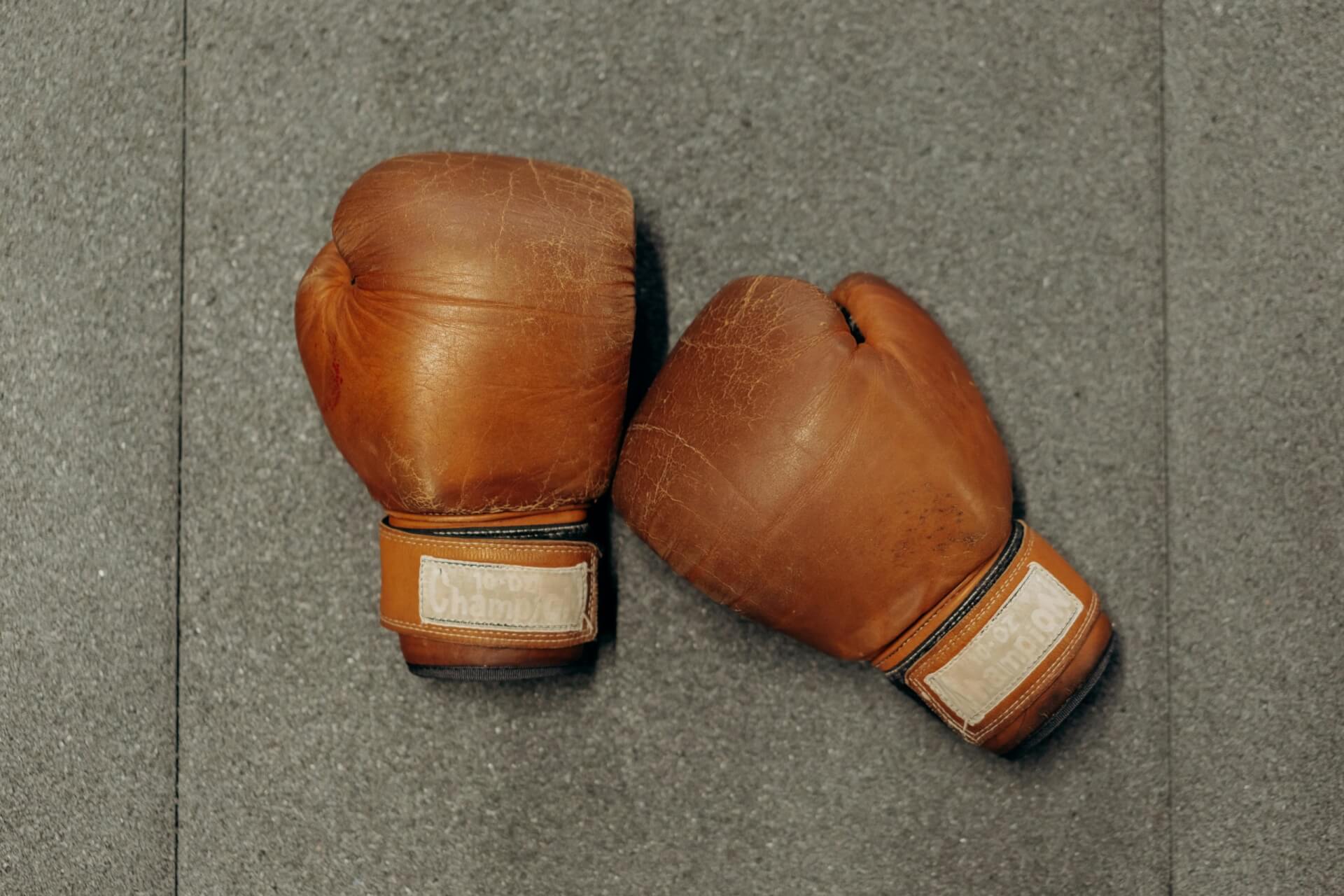 Anciens gants de boxe en cuir marron sur fond gris.